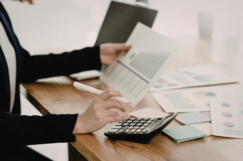 Person reviewing financial documents at a desk with graphs, calculator, and laptop, analyzing business data.