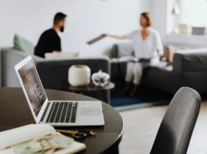 Two people seated in a modern office setting during a client onboarding meeting, with a laptop, notebook, and currency notes on the table in the foreground.