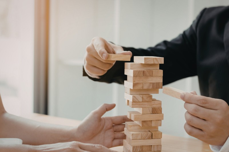 Hands removing blocks from a Jenga tower, symbolizing a system becoming unstable as more weight is added.