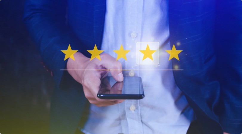 Person holding a smartphone with a five‑star rating graphic displayed in front of them.