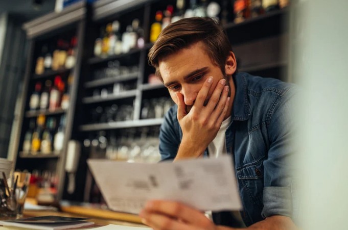 A business owner reviewing paperwork at a counter, focusing closely on financial details — representing the moment when numbers stop matching day‑to‑day reality.