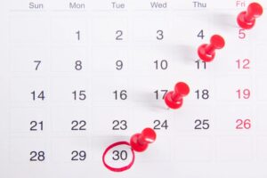 A monthly calendar with several dates marked by red push pins and the 30th circled in red.