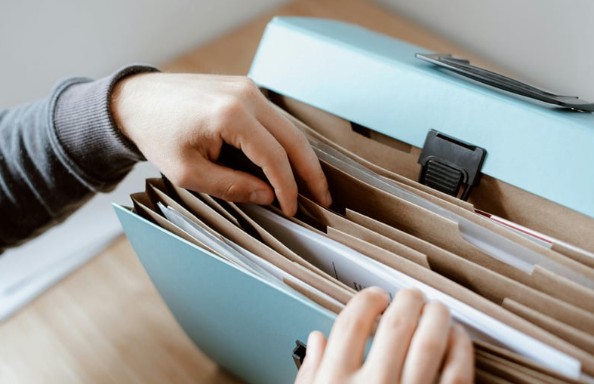 Hands sorting through an accordion file filled with older documents and folders.