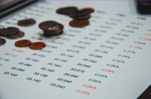 Coins scattered across a printed financial report showing rows of numbers and percentage variances in red and black